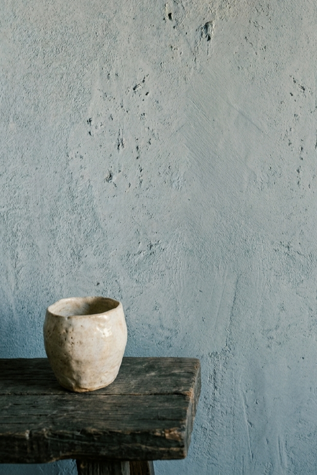 Detail of a muted dusty blue limewash wall texture with warm timber furniture in the foreground. Dark Japandi feature wall idea.